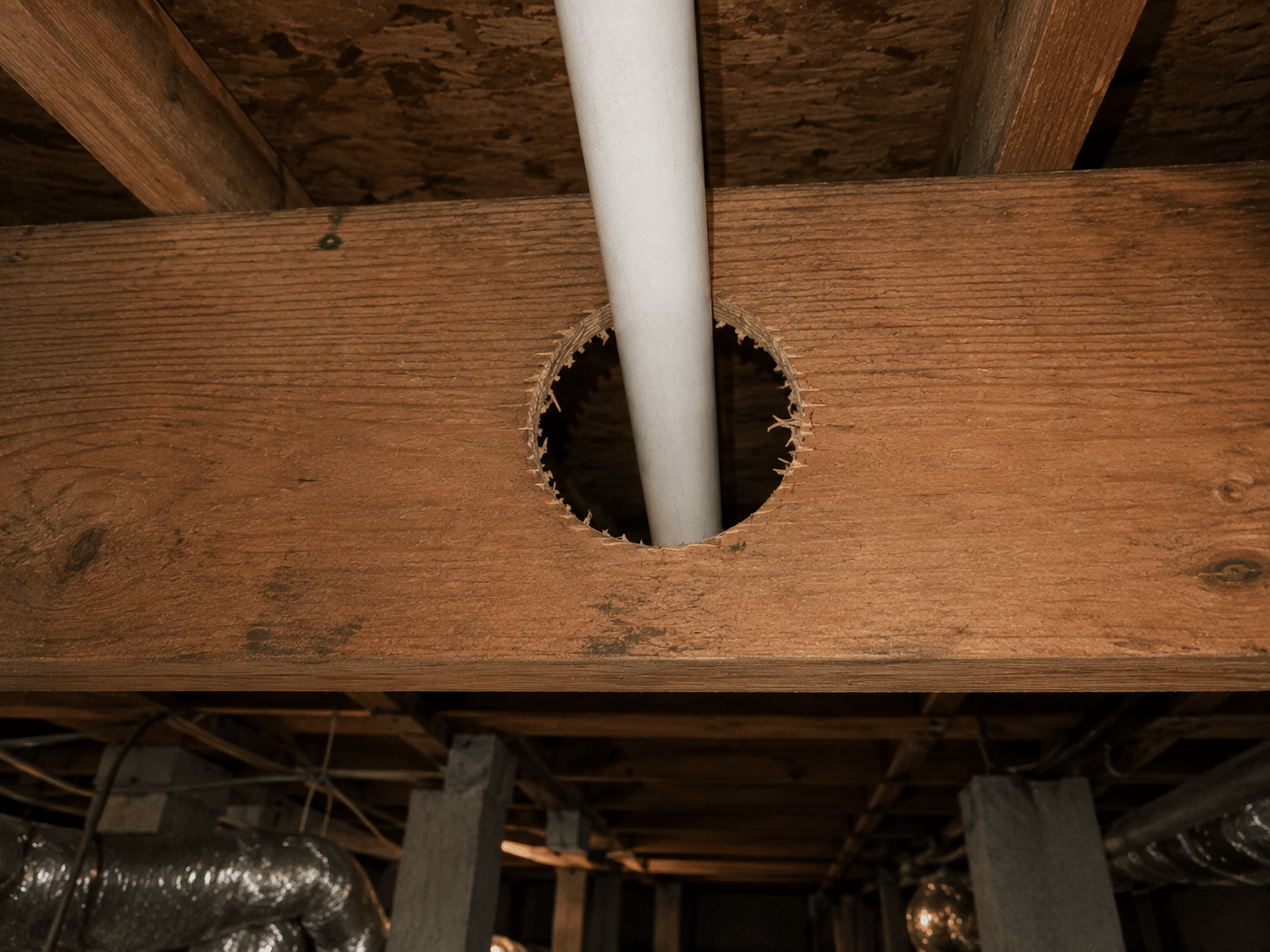 Oversized hole cut through the center of a wood floor joist for a PVC pipe, before repair