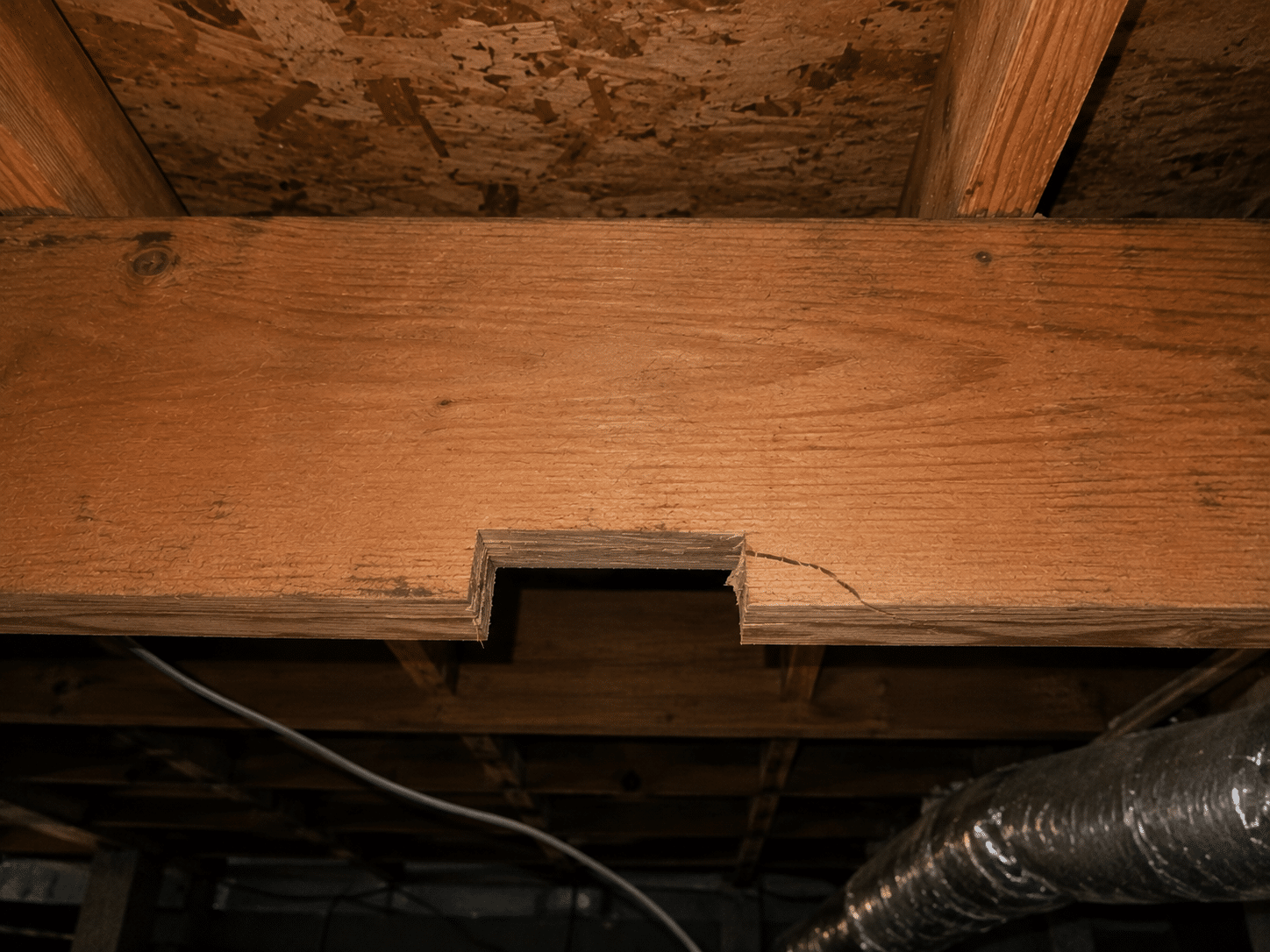 Notch cut into the bottom edge of a wood floor joist, with a crack extending from the corner, before repair