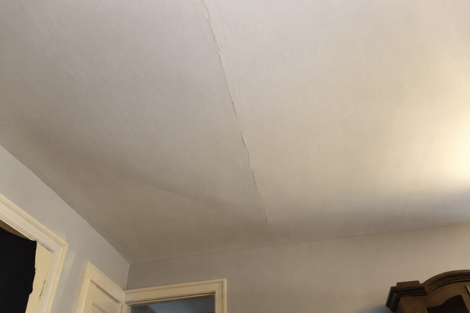 Hairline crack in painted ceiling drywall, a common warning sign of a damaged floor joist above