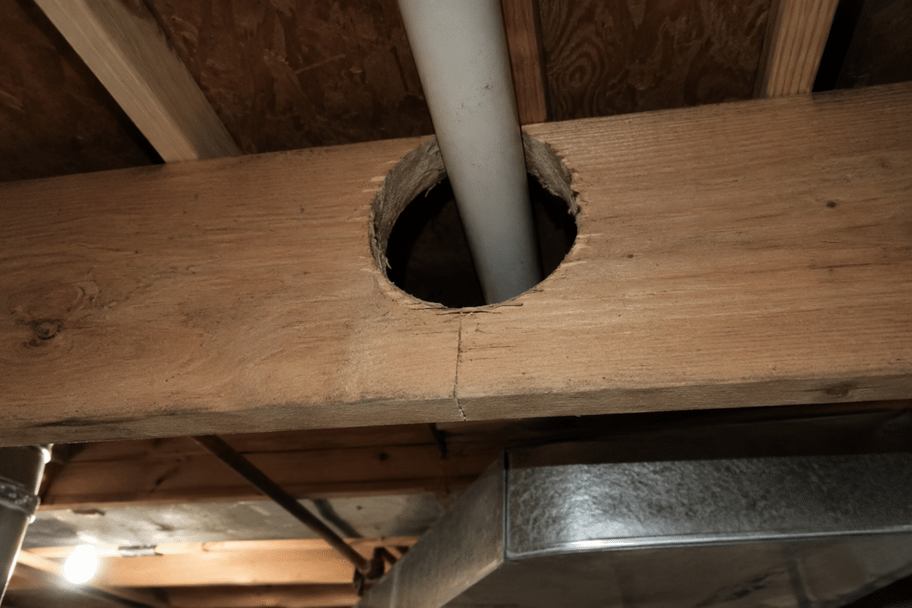 Oversized hole cut through a wood floor joist for a PVC pipe, before repair